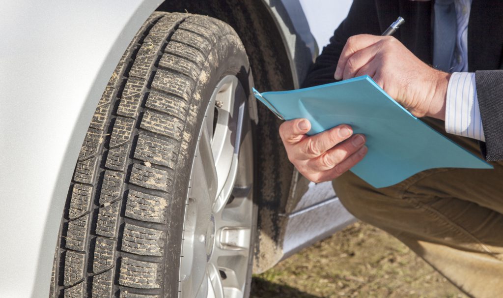 Man with paper block kneeling on car tires Fleet Tech